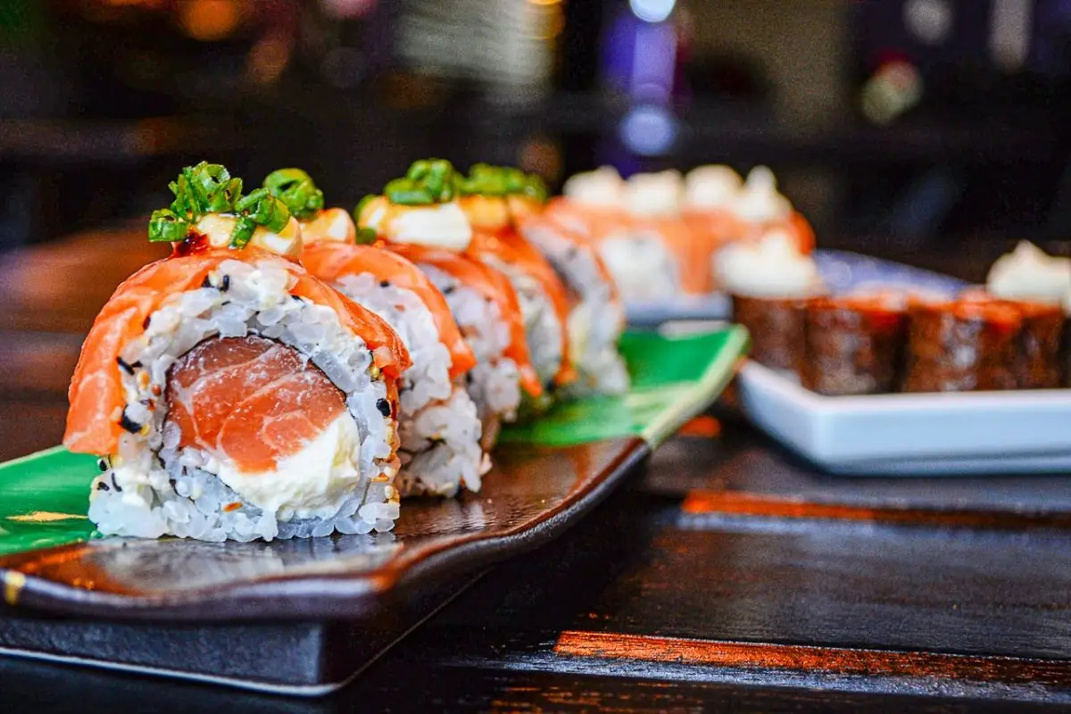 pexels-photo-3620705 Delicious sushi rolls with salmon and cream cheese garnished with green onions, presented on a ceramic plate.